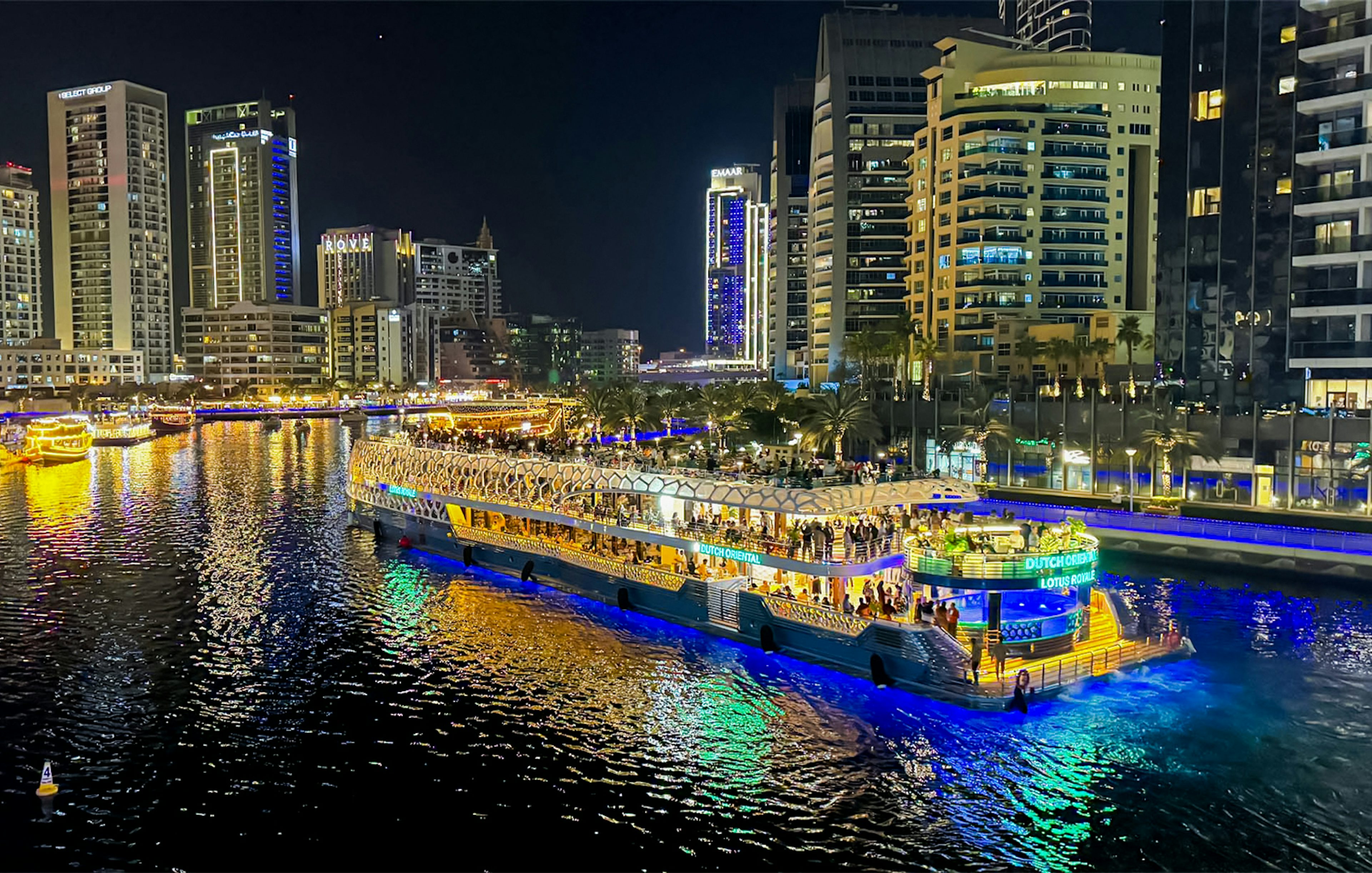 Nighttime cruise on illuminated waterway with city skyline in the background.