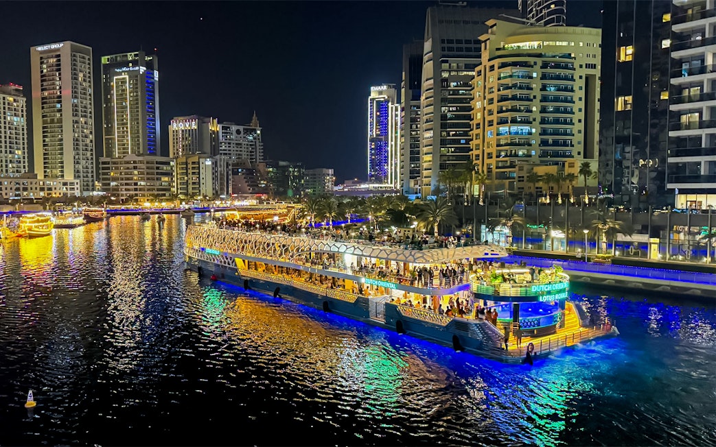 Nighttime cruise on illuminated waterway with city skyline in the background.