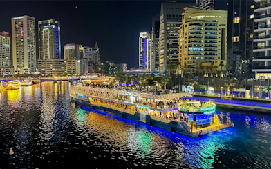 Nighttime cruise on illuminated waterway with city skyline in the background.