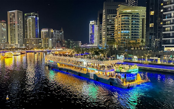 Nighttime cruise on illuminated waterway with city skyline in the background.
