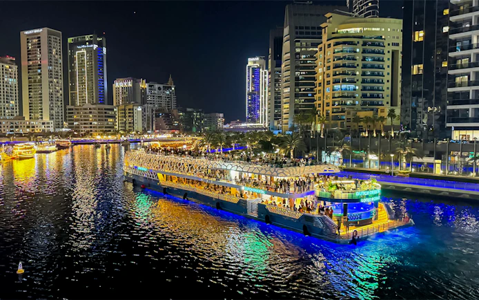 Nighttime cruise on illuminated waterway with city skyline in the background.