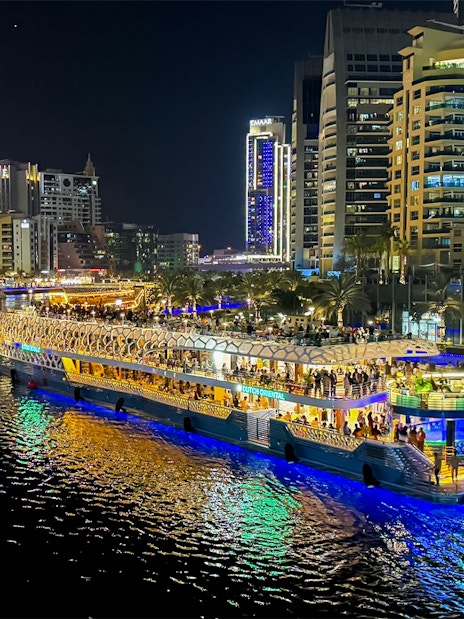 Nighttime cruise on illuminated waterway with city skyline in the background.