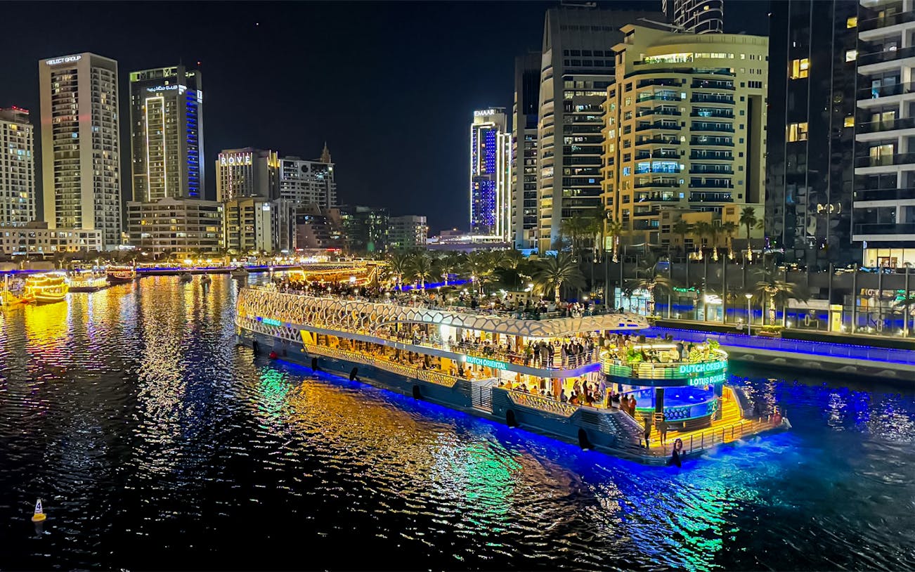 Nighttime cruise on illuminated waterway with city skyline in the background.