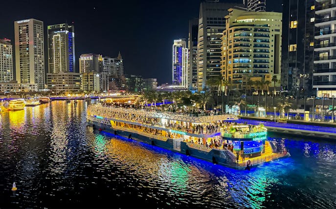 Nighttime cruise on illuminated waterway with city skyline in the background.