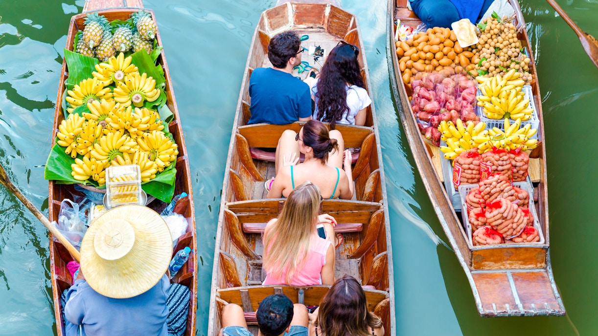 Boats with tourists and vendors selling fruit at Amphawa Floating Market, Thailand.