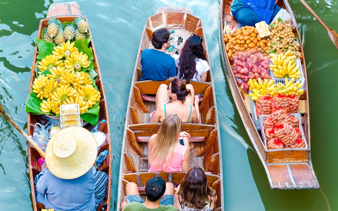 Boats with tourists and vendors selling fruit at Amphawa Floating Market, Thailand.