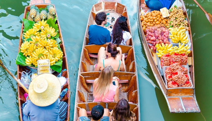 Boats with tourists and vendors selling fruit at Amphawa Floating Market, Thailand.