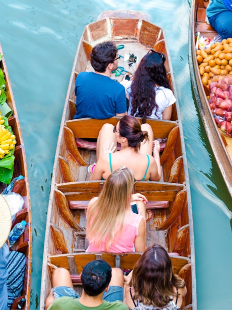 Boats with tourists and vendors selling fruit at Amphawa Floating Market, Thailand.