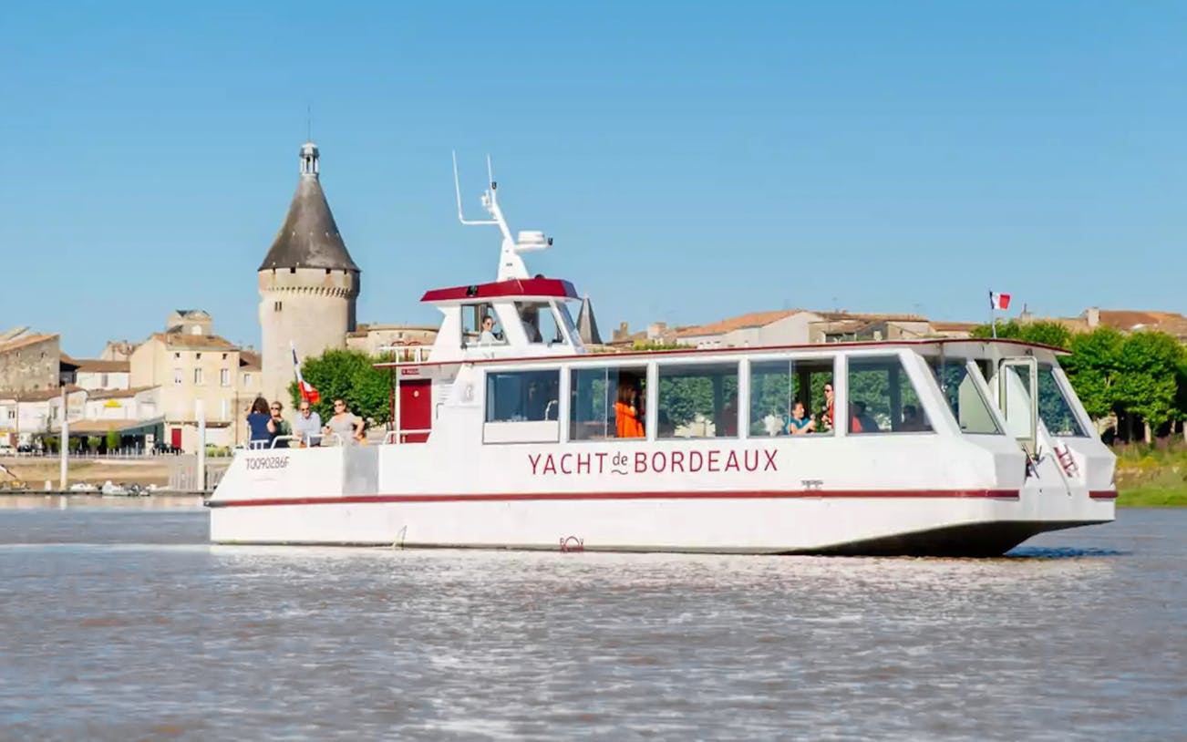 Cruise boat on Bordeaux river with historic tower in background.