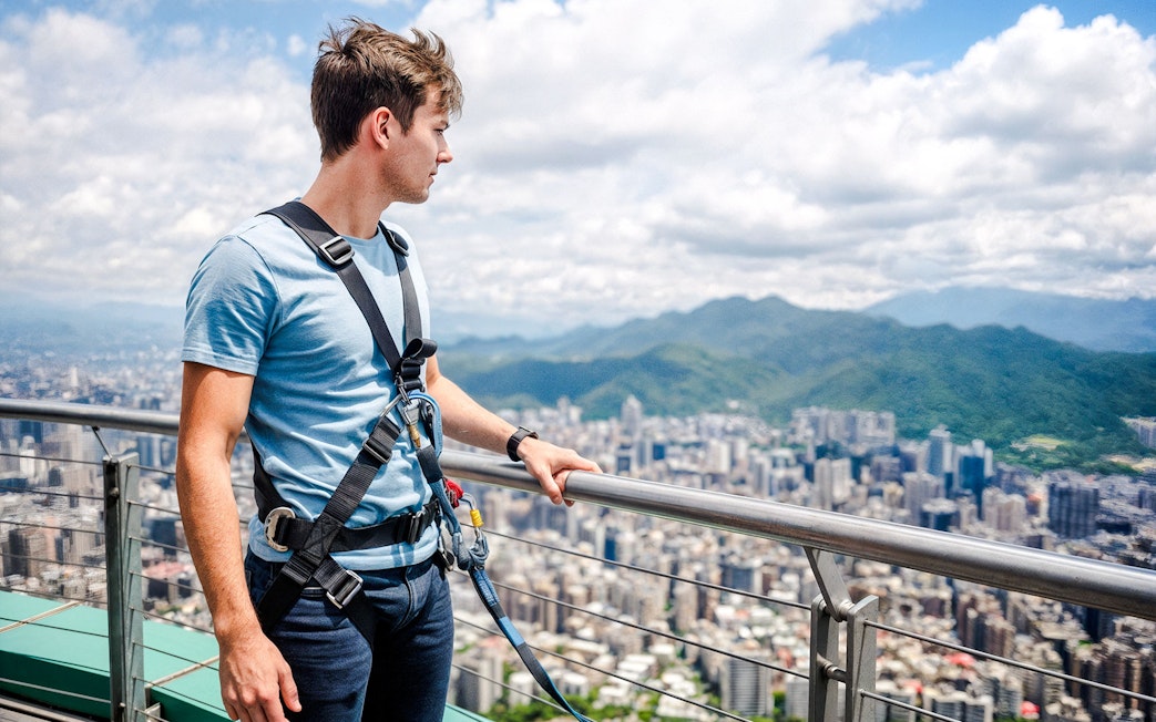 Man on Taipei 101 observation deck with cityscape and mountains in background.