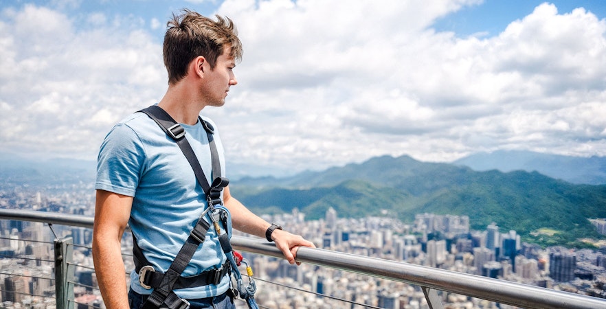 Man on Taipei 101 observation deck with cityscape and mountains in background.