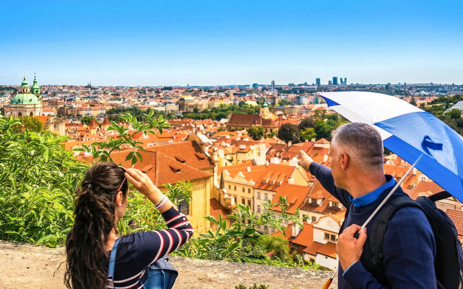 Panoramic view of Prague's historic red-tiled roofs with tourists overlooking the city.