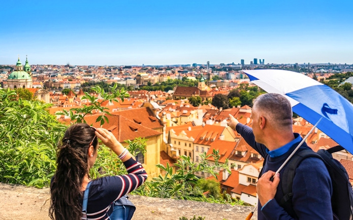 Panoramic view of Prague's historic red-tiled roofs with tourists overlooking the city.