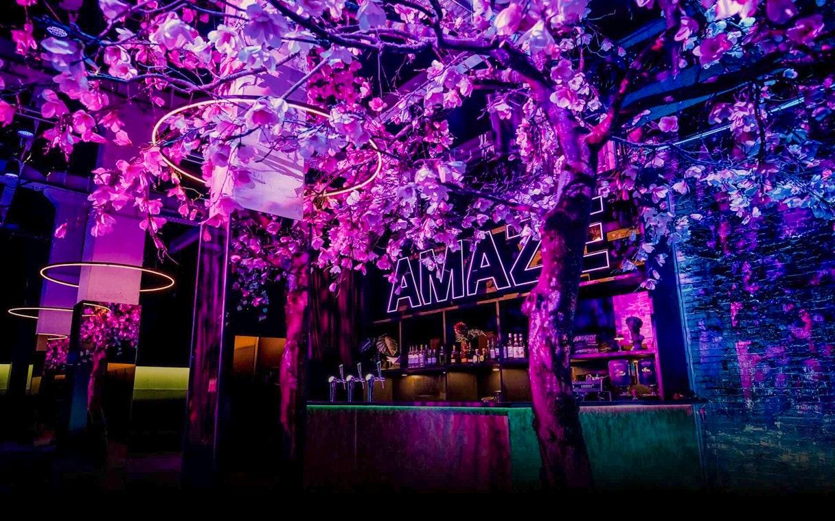 Amaze Amsterdam bar with neon lights and floral decor.