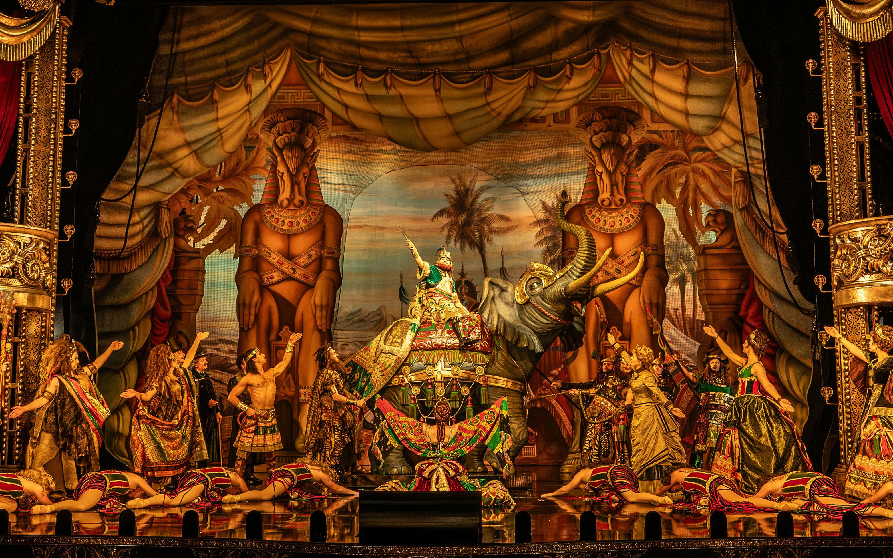 Stage scene from Phantom production with performers in elaborate costumes and an elephant prop.