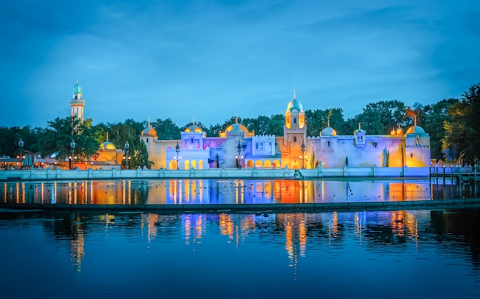 Efteling theme park illuminated at night, reflecting on water in Amsterdam.