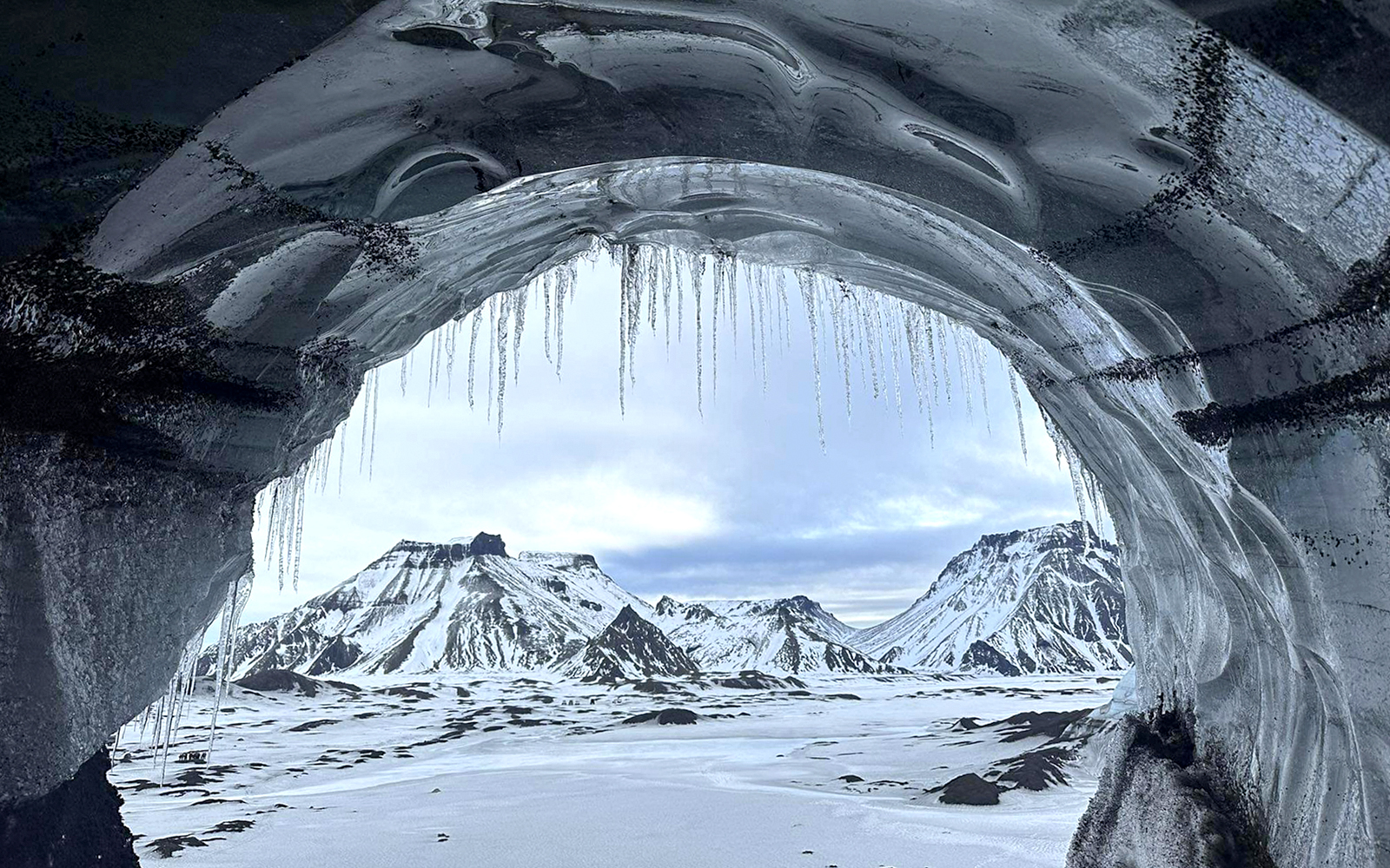 View from inside Katla Ice Cave, Iceland, showing snow-covered mountains.