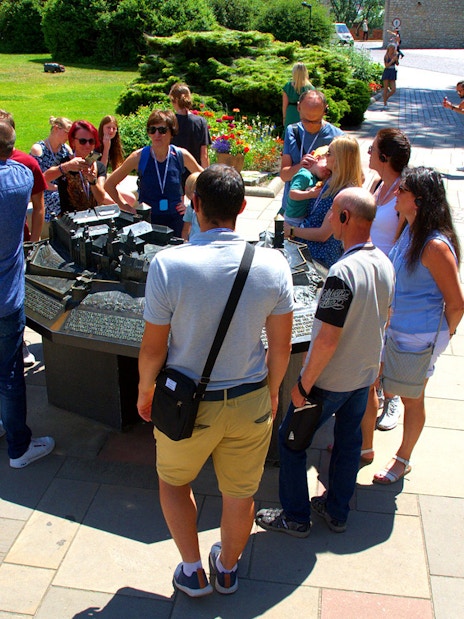 Group of tourists on a guided tour at Wawel Castle, viewing a model of the castle grounds.
