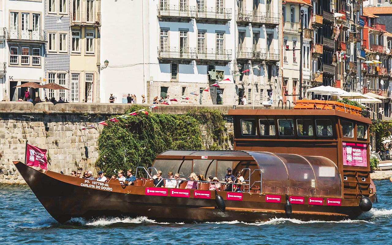 Tourists on a sightseeing boat at Douro Pier, Porto, with historic buildings in the background.