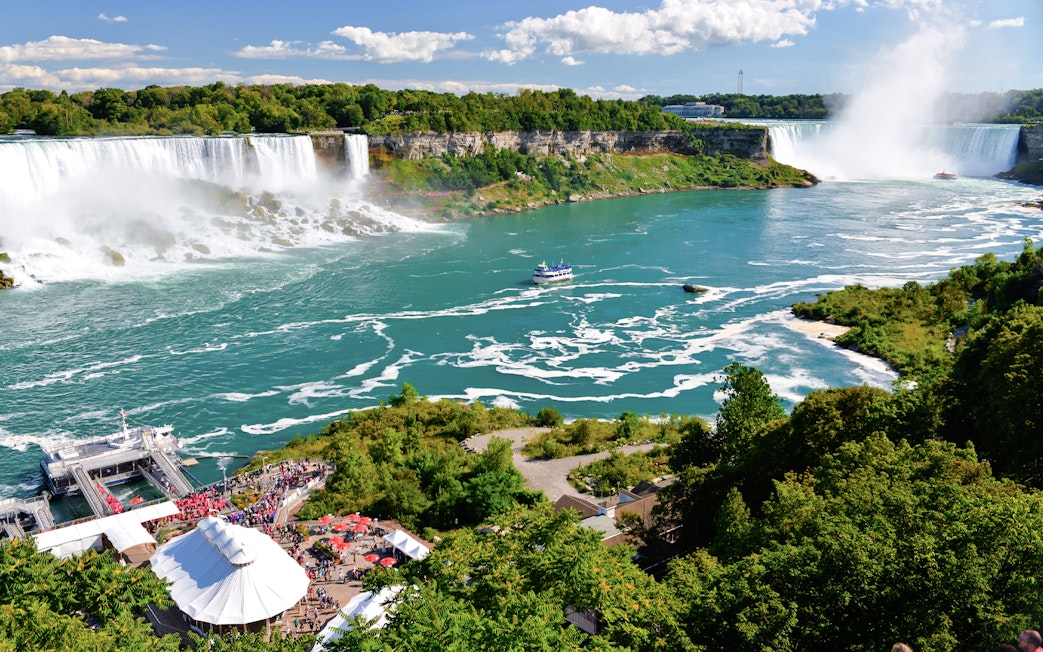 Niagara Falls with American and Bridal Veil Falls, boat on river, lush greenery.