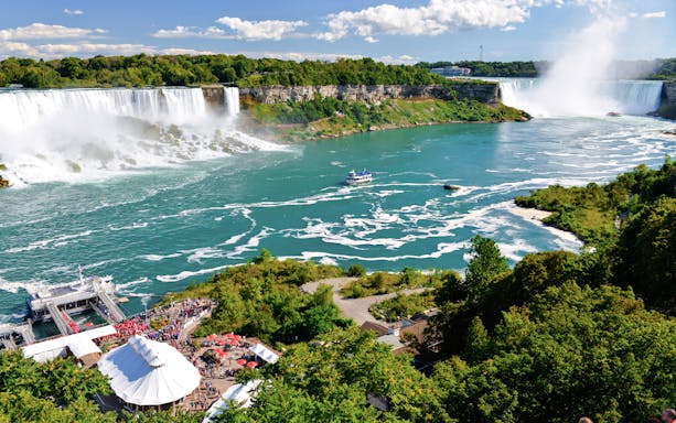 Niagara Falls with American and Bridal Veil Falls, boat on river, lush greenery.