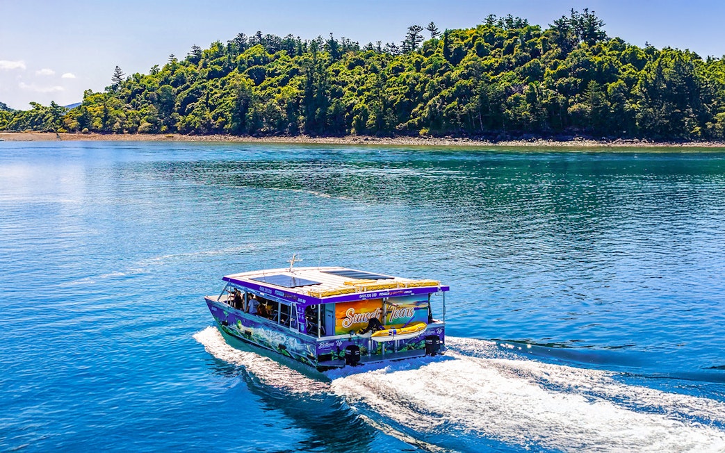 Glass bottom boat cruising near lush island at Airlie Beach.