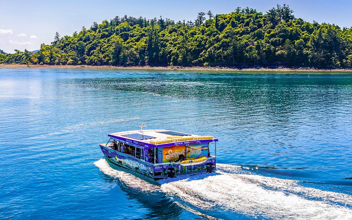 Glass bottom boat cruising near lush island at Airlie Beach.
