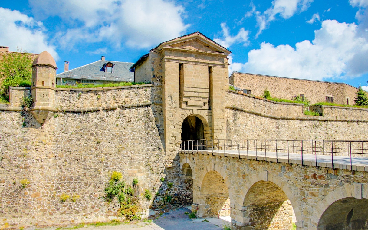Forteresse de Montlouis stone entrance with arched bridge under a blue sky.