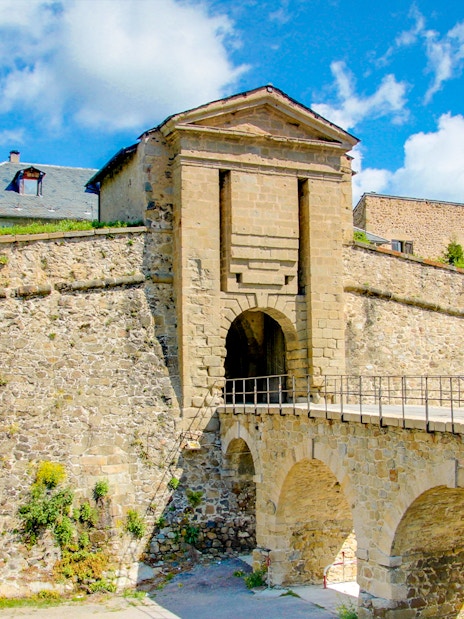Forteresse de Montlouis stone entrance with arched bridge under a blue sky.