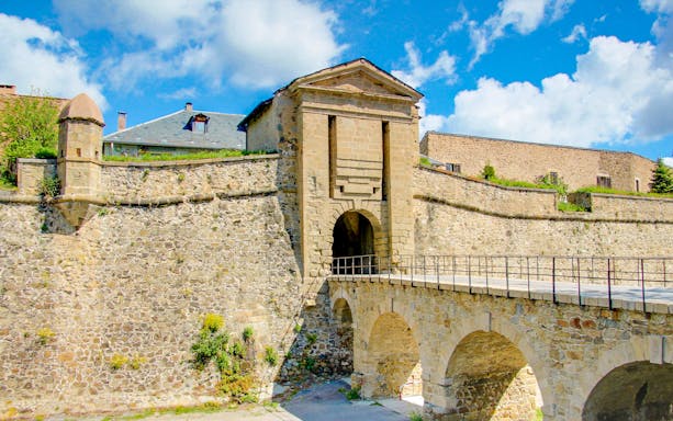 Forteresse de Montlouis stone entrance with arched bridge under a blue sky.