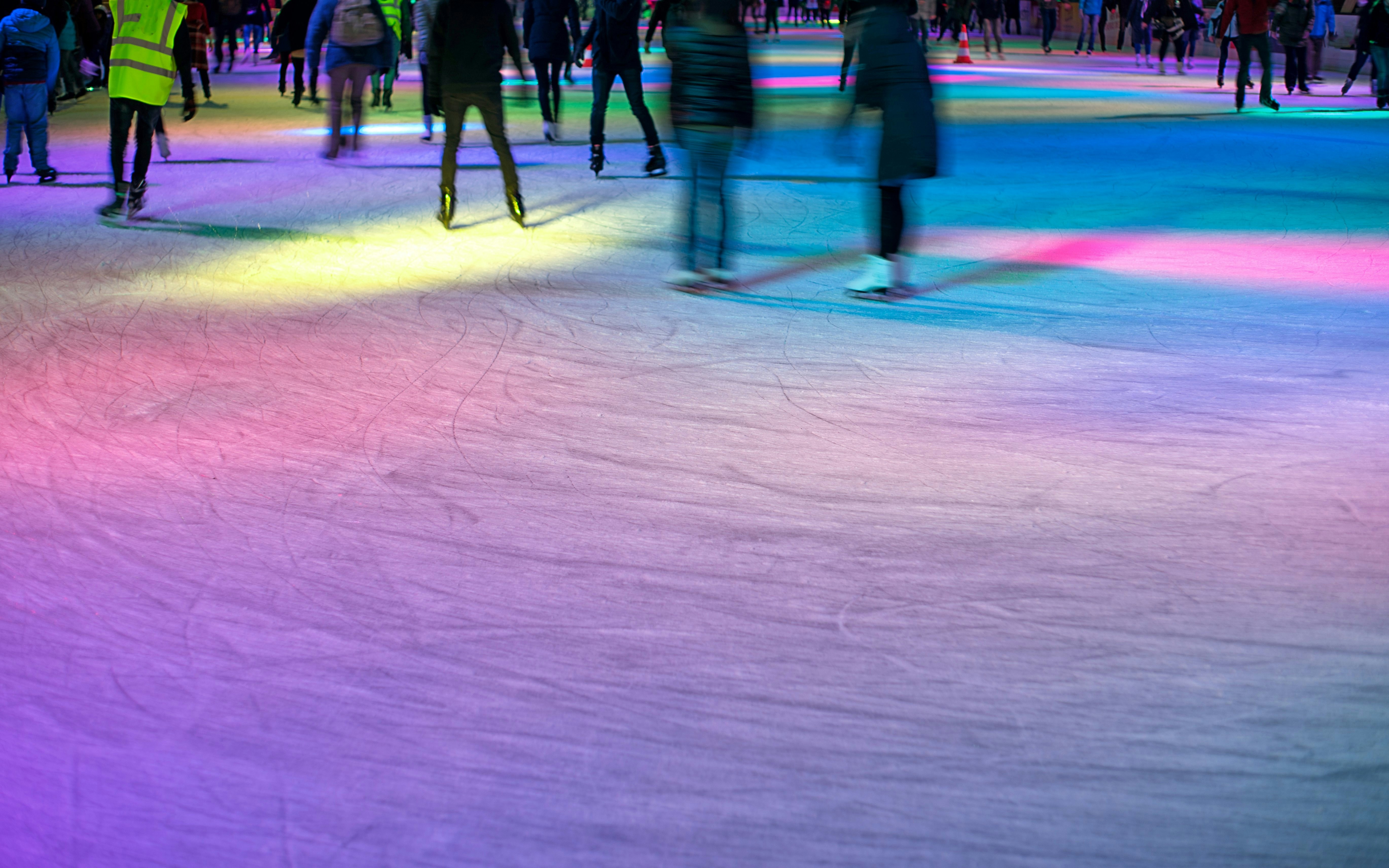 Nighttime ice skating with colorful lights on a crowded rink.