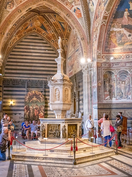 Tourists inside Siena Cathedral admiring frescoes and architecture, Italy.