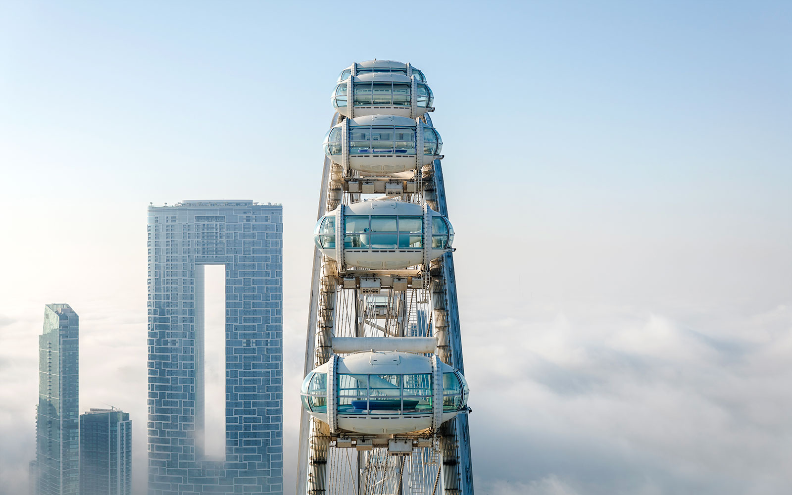 Ain Dubai pods above the clouds with city skyscrapers in the background.