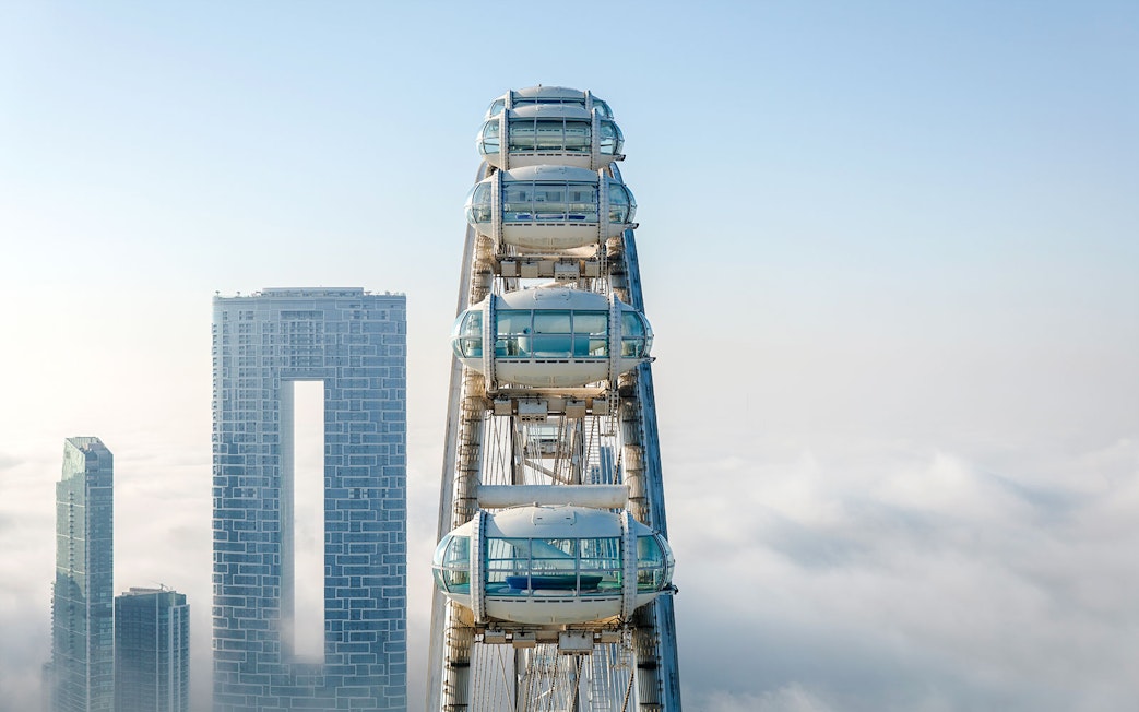 Ain Dubai pods above the clouds with city skyscrapers in the background.