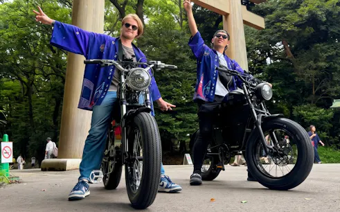 Two people on e-bikes in front of a large wooden gate, wearing blue jackets, enjoying a ride.