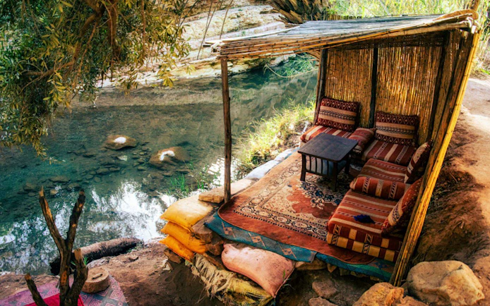 Seating area by a stream in Paradise Valley with cushions and a bamboo shelter.