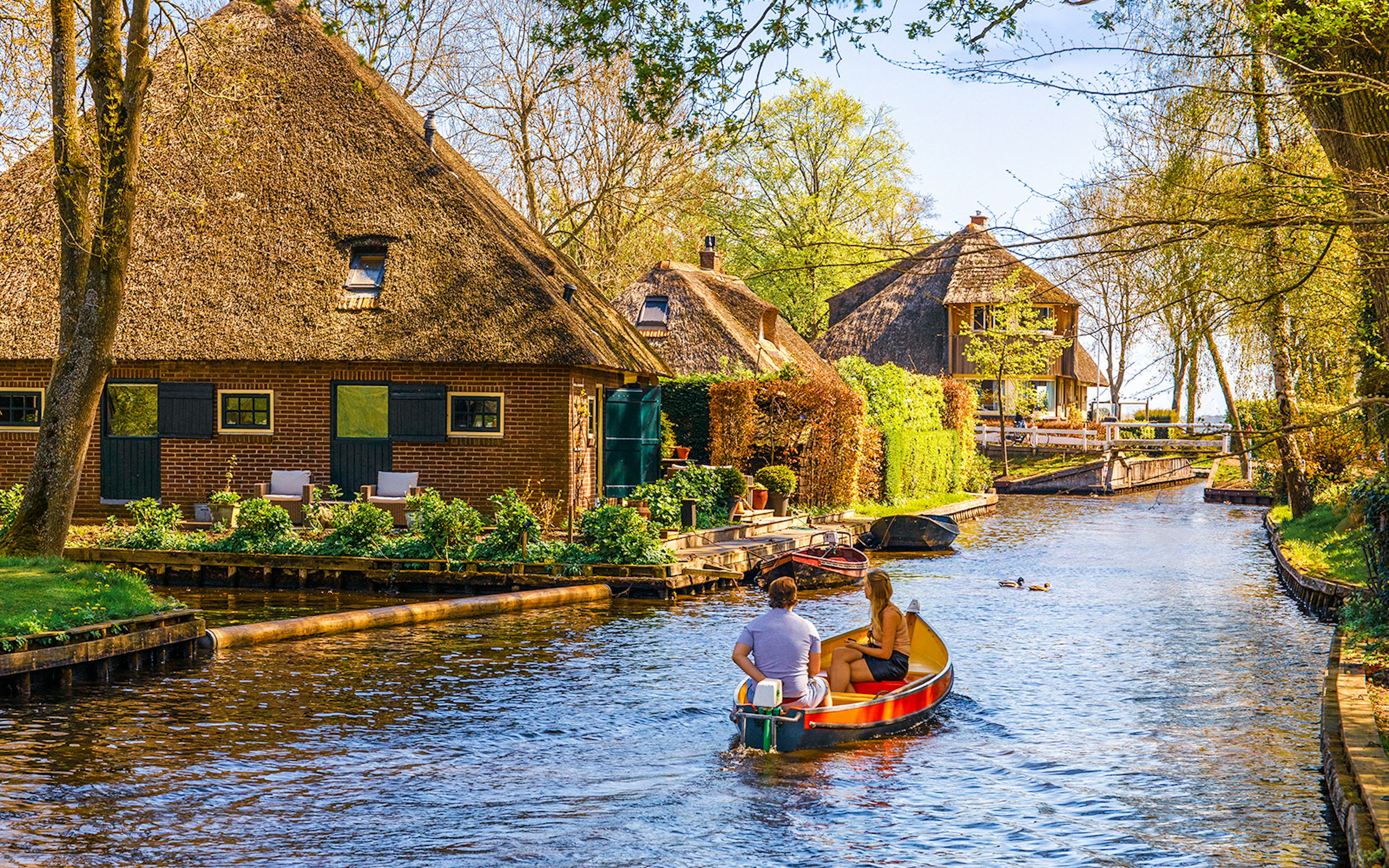 Boating through Giethoorn canal with thatched houses and lush greenery, Giethoorn, Netherlands.