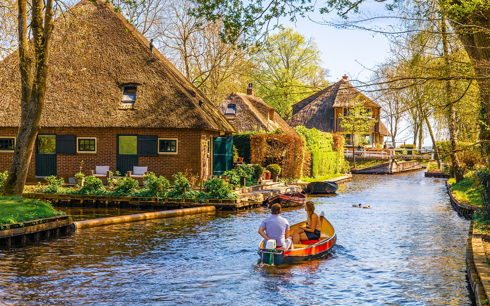 Boating through Giethoorn canal with traditional houses and lush greenery, Giethoorn, Netherlands.
