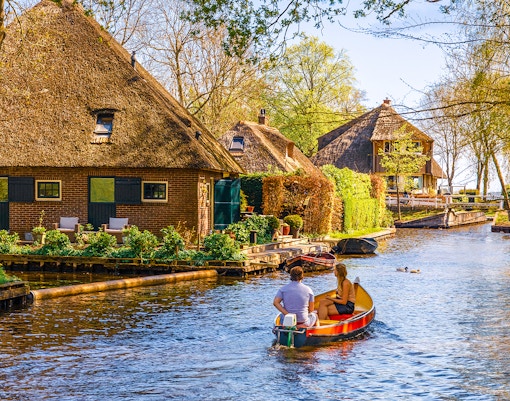 Boating through Giethoorn canal with thatched houses and lush greenery, Giethoorn, Netherlands.