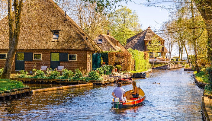 Boating through Giethoorn canal with thatched houses and lush greenery, Giethoorn, Netherlands.