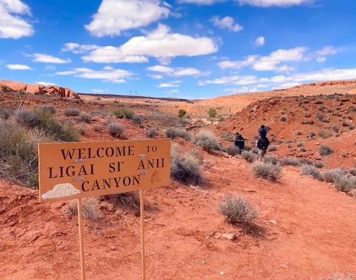 Welcome sign at Ligai Si Anii Canyon with horseback riders on red desert trail.
