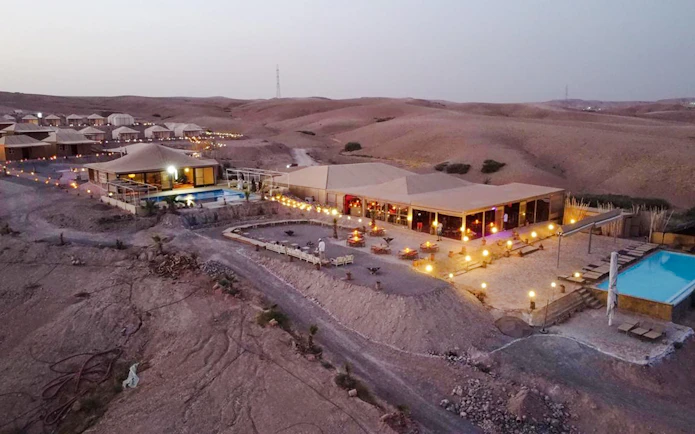 Desert camp with tents and pool in Agafay near Marrakesh at dusk.