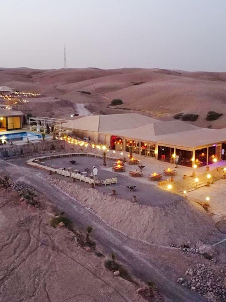 Desert camp with tents and pool in Agafay near Marrakesh at dusk.