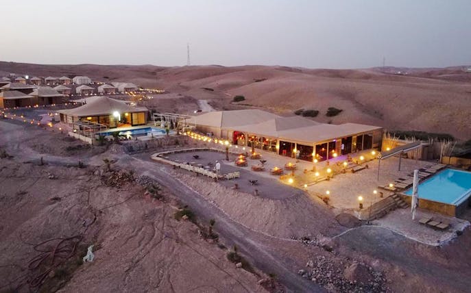 Desert camp with tents and pool in Agafay near Marrakesh at dusk.