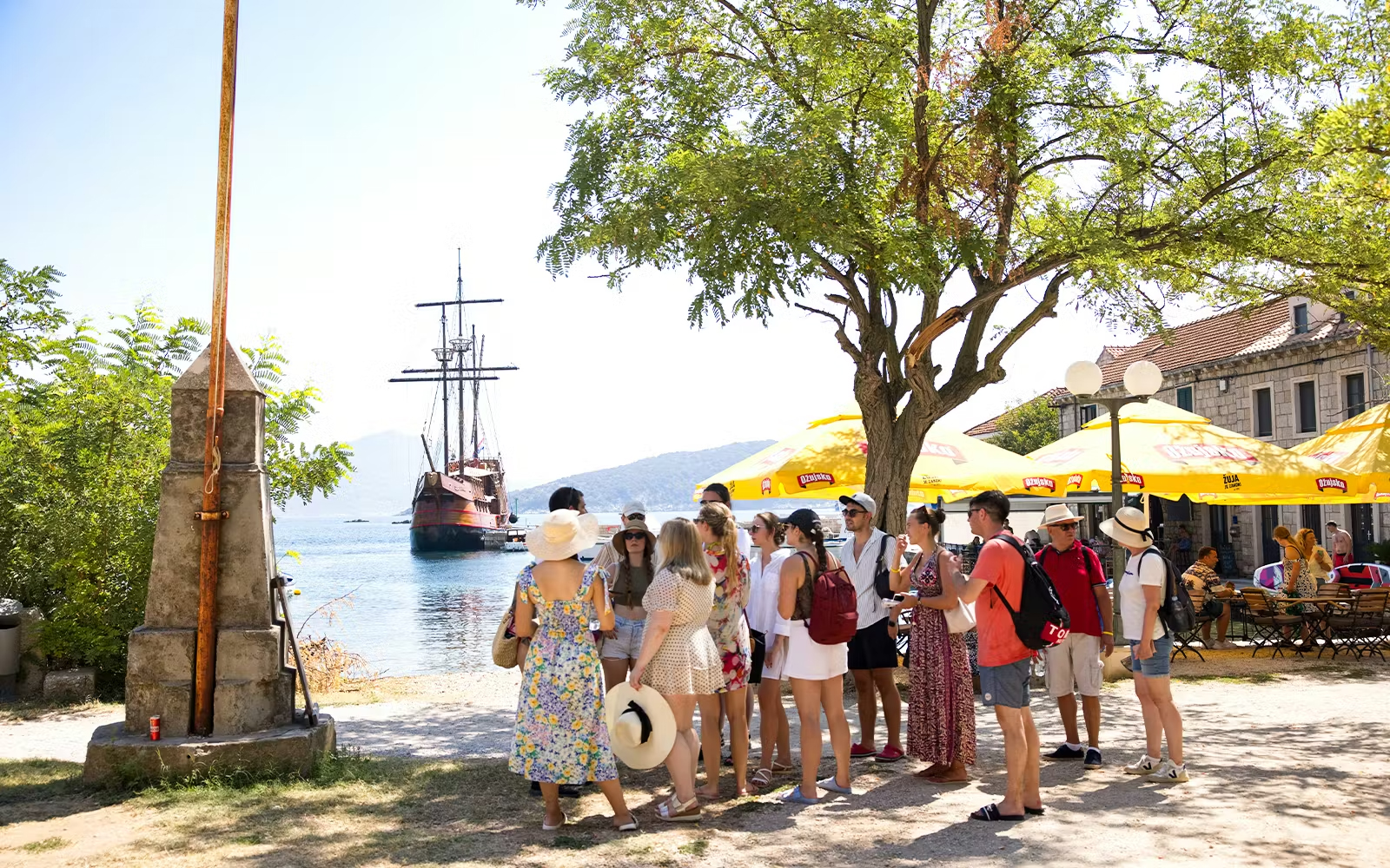 Guests exploring Elaphite Island with Karaka ship in the background during Elaphite Islands Cruise.
