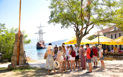 Guests exploring Elaphite Island with Karaka ship in the background during Elaphite Islands Cruise.