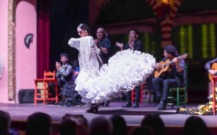 Flamenco dancer in white dress performing on stage with musicians in background.