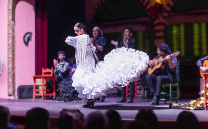 Flamenco dancer in white dress performing on stage with musicians in background.