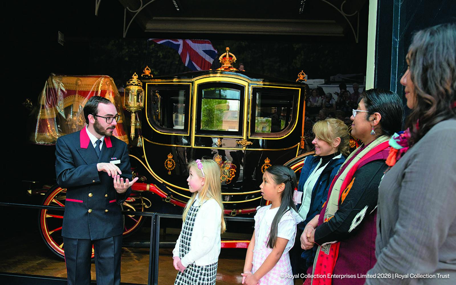 Guide explaining royal carriage to visitors at Royal Mews, London.