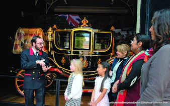 Guide explaining royal carriage to visitors at Royal Mews, London.